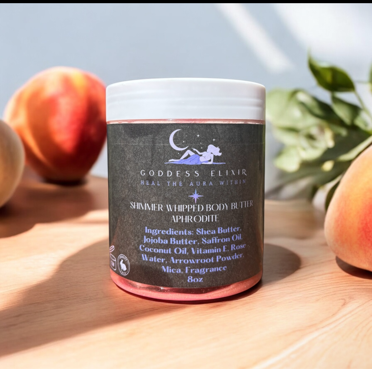 Jar of Goddess Elvir body butter on a wooden surface with peaches and plants in the background