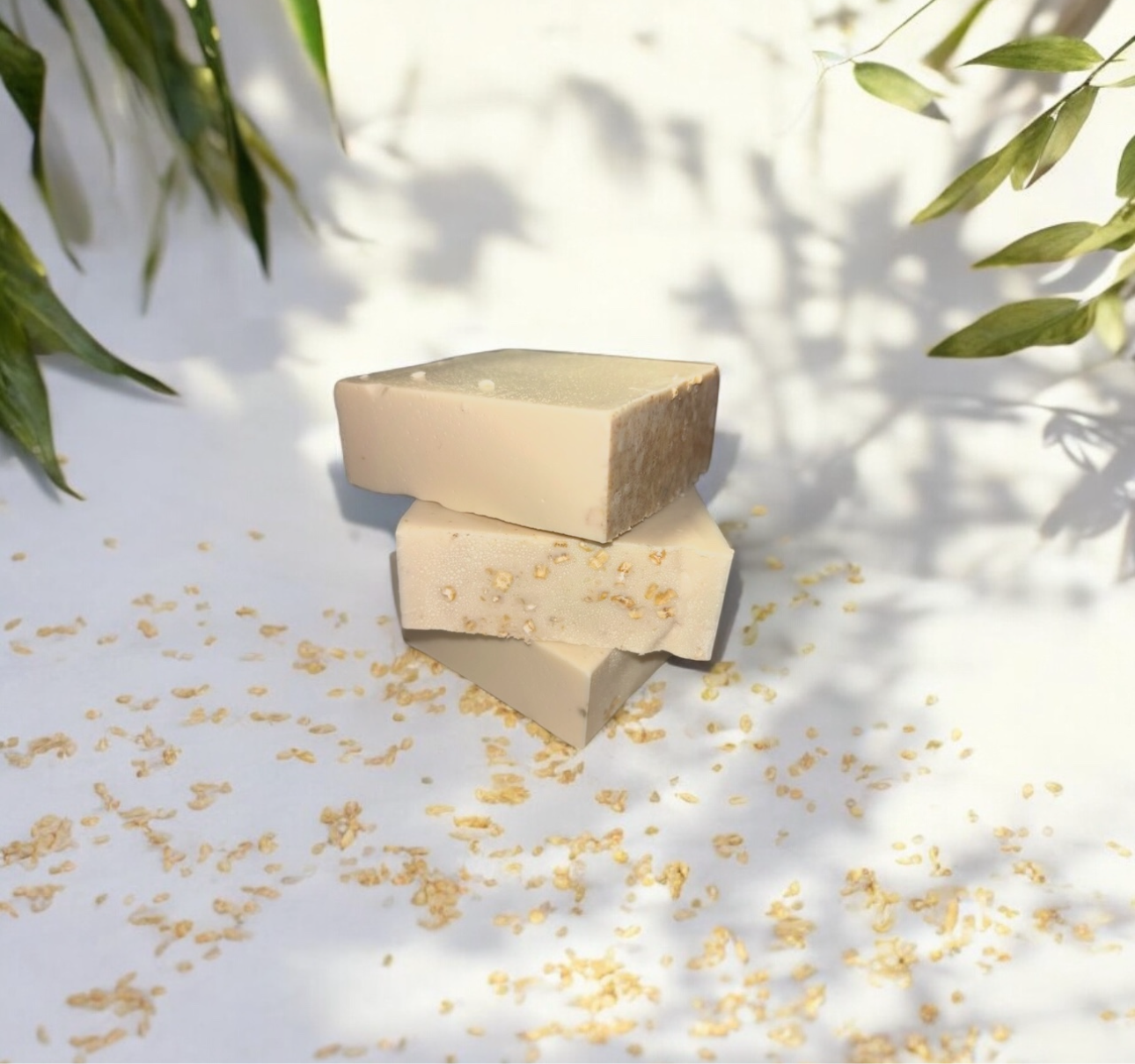 Two stacked soap bars on a light surface with green leaves in the background