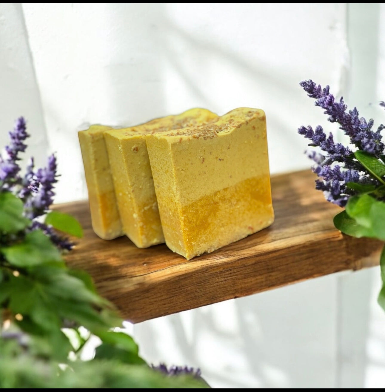 Three yellow soap bars on a wooden board with lavender flowers in the background